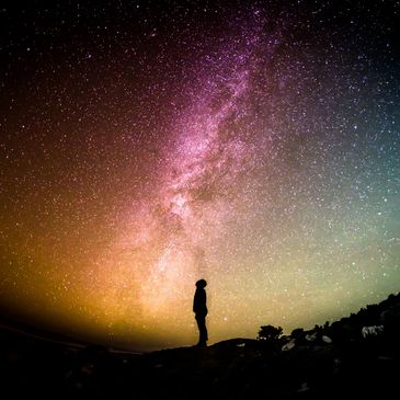 The silhouette of  a person stands under the Milky Way galaxy, gazing up.