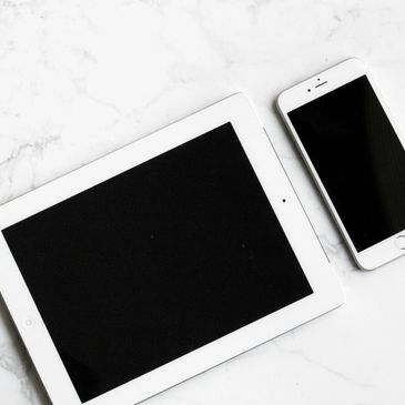 An Apple iPad and iPhone 6 Plus, both white, placed on a complementary white granite background.