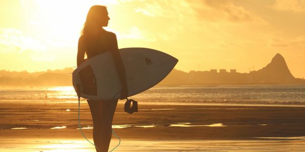 Lady with surf board looking off into the sunset.