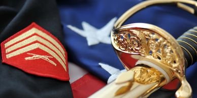 Marine Corps uniform with sergeant strips and NCO sword laid on top of the American flag