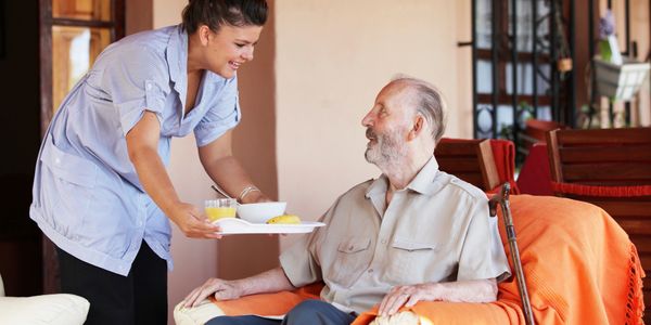 Caregiver serving tea to an elderly man in his home