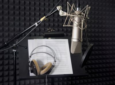 Professional record microphone and headphones with a background portraying a recording booth.