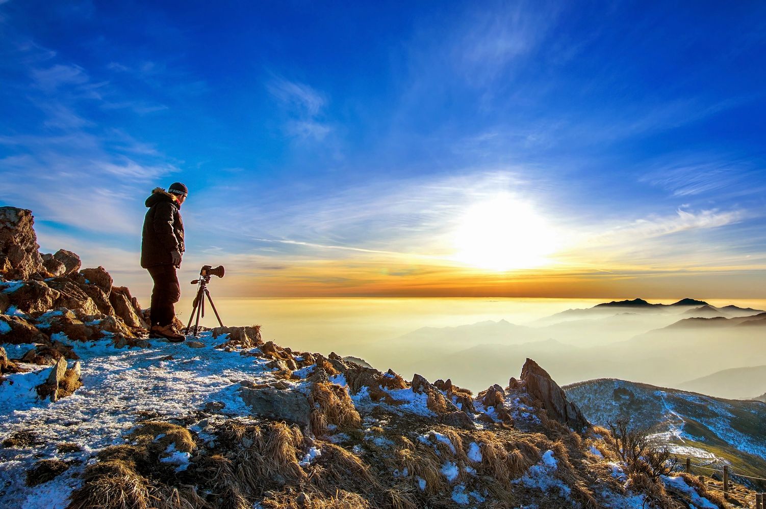 Man with tripod camera on top of a mountain looking out into infinity