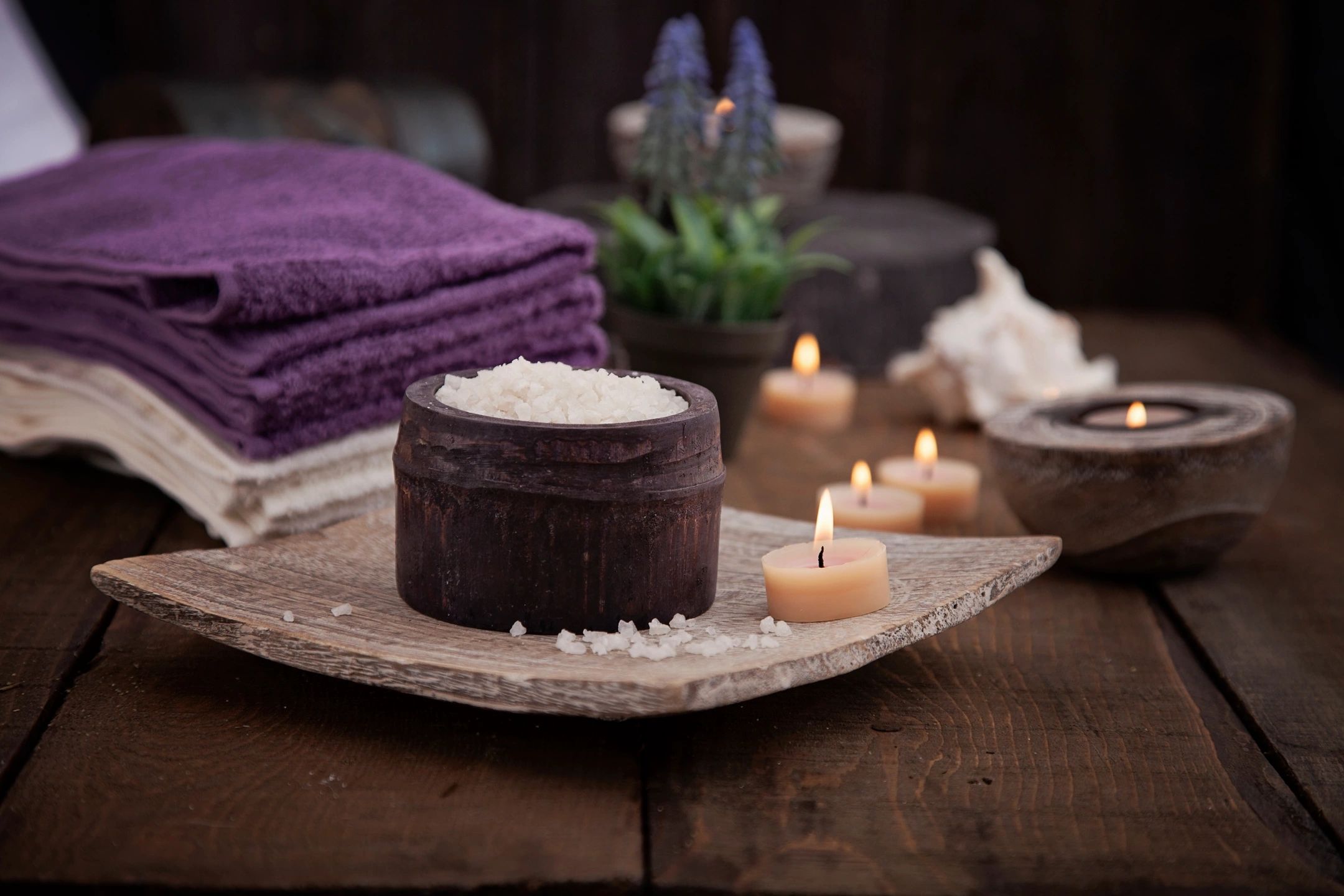 relaxing spa setting with mini candles, plush towels on wood plank and bath salts