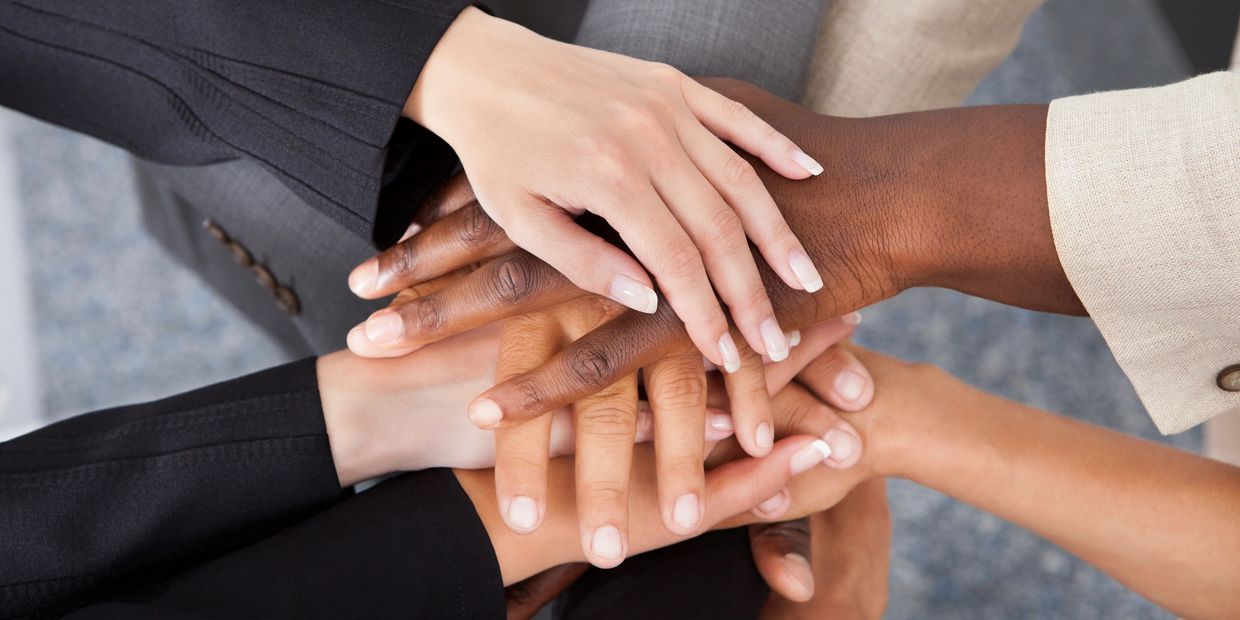 Multiple hands of diverse skin colours. They are grasped and stacked on top of each other