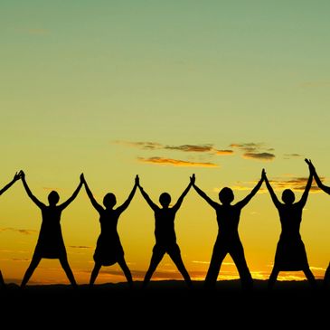 Seven people standing beside each other in front of a sunset with their hands held up