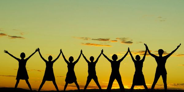 silhouette of 7 people raising their hands in celebration, against a sunrise