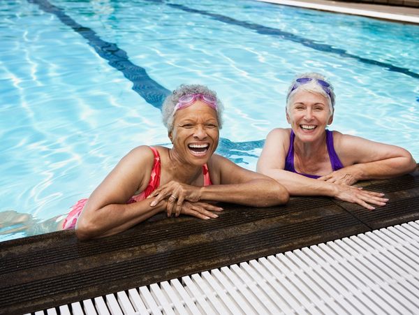 Two lovely senior women smiling and laughing after their pool rehab, at edge of pool