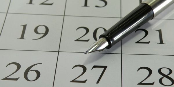 A fountain pen lays atop a calendar