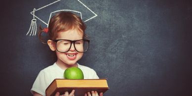 Young pre-school girl standing against the blackboard holding an apple