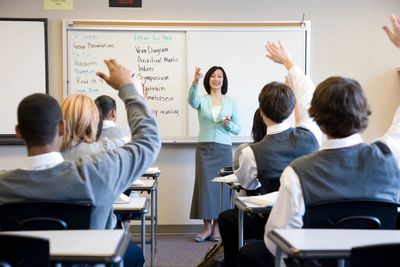 A teacher taking a class. Students raising their hands to answer a question. 