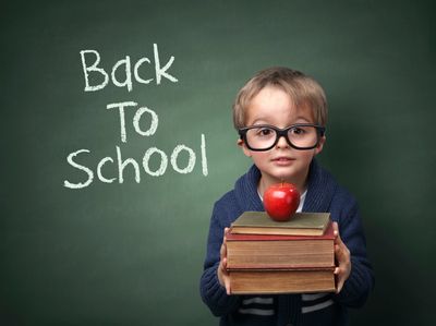 Child wearing blue sweater & black glasses holding 3 books & 1 apple with back to school chalkboard.
