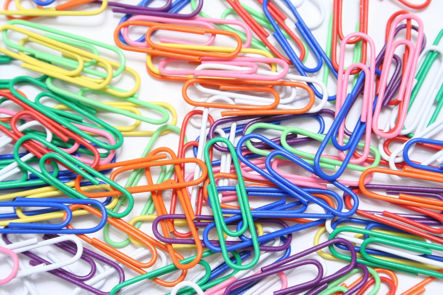 A large number of different coloured paperclips spread out.