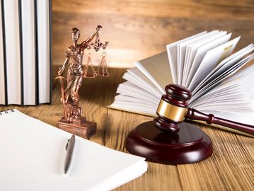 books, open book, lady justice, gavel, notebook and pen on a table