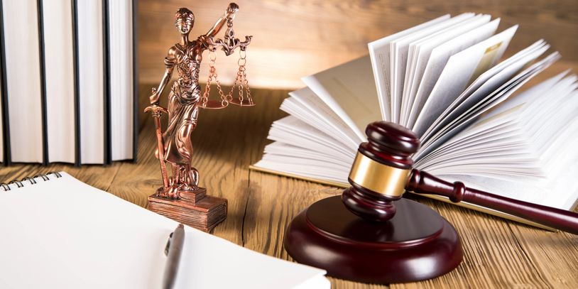 Picture of a note pad, books, statue of lady justice and a gavel on a desk.