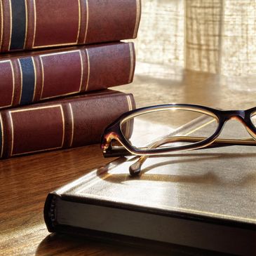 Law books in the background and a pair of glasses on top of a book in the foreground
