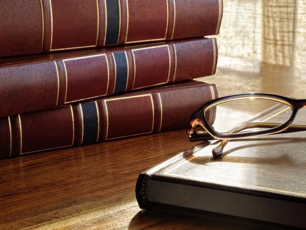 A stack of law books and a book with folded glasses on top of it resting on it on a wooden table. 