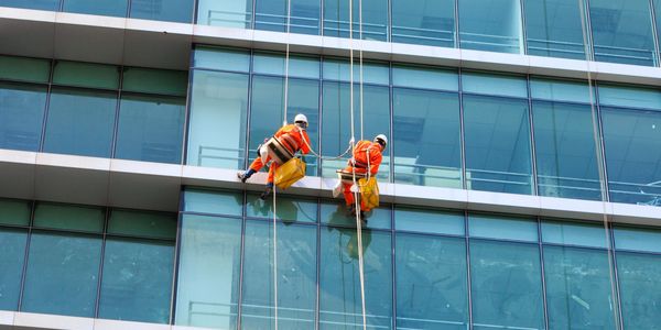 Dos operarios de limpieza, encargándose de limpiado de vidrios exteriores de un edificio 