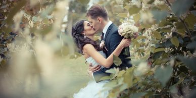 A picture of a bride and groom in the forest embracing each other and kissing. 