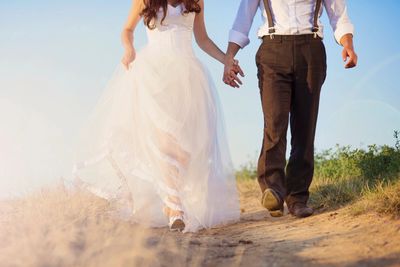 Bride and groom walking on beach with blue sky and green grass in background