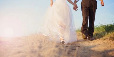 A photograph of a bride and a groom walking on a beach.