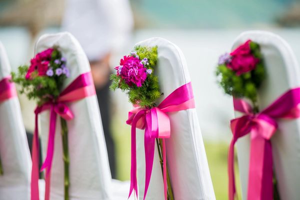 A row of chairs decorated in pink ribbon, flowers, and white chair covers.