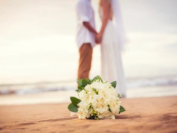 White bouquet on beach in front of wedding couple. Where to have destination wedding. Wedding travel