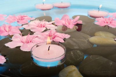 Floating candles in water with with smooth black stones and pink flowers.