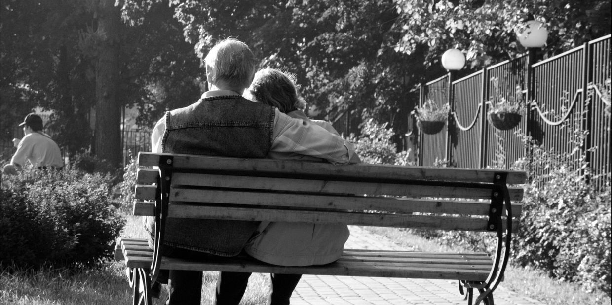 A husband & wife sitting on a park bench looking at nature.