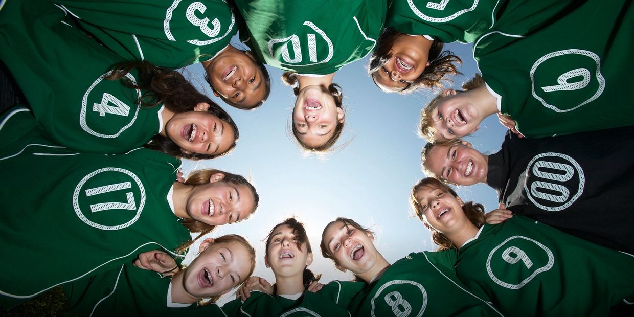 A sport's team members huddled in a circle wearing green shirts with a number on it. 
