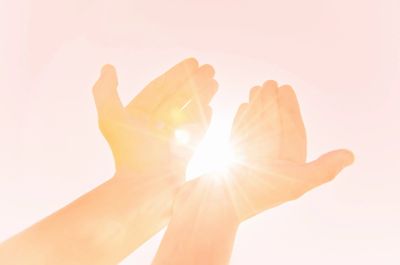 Two hands are held open with a beam of light passing between them.