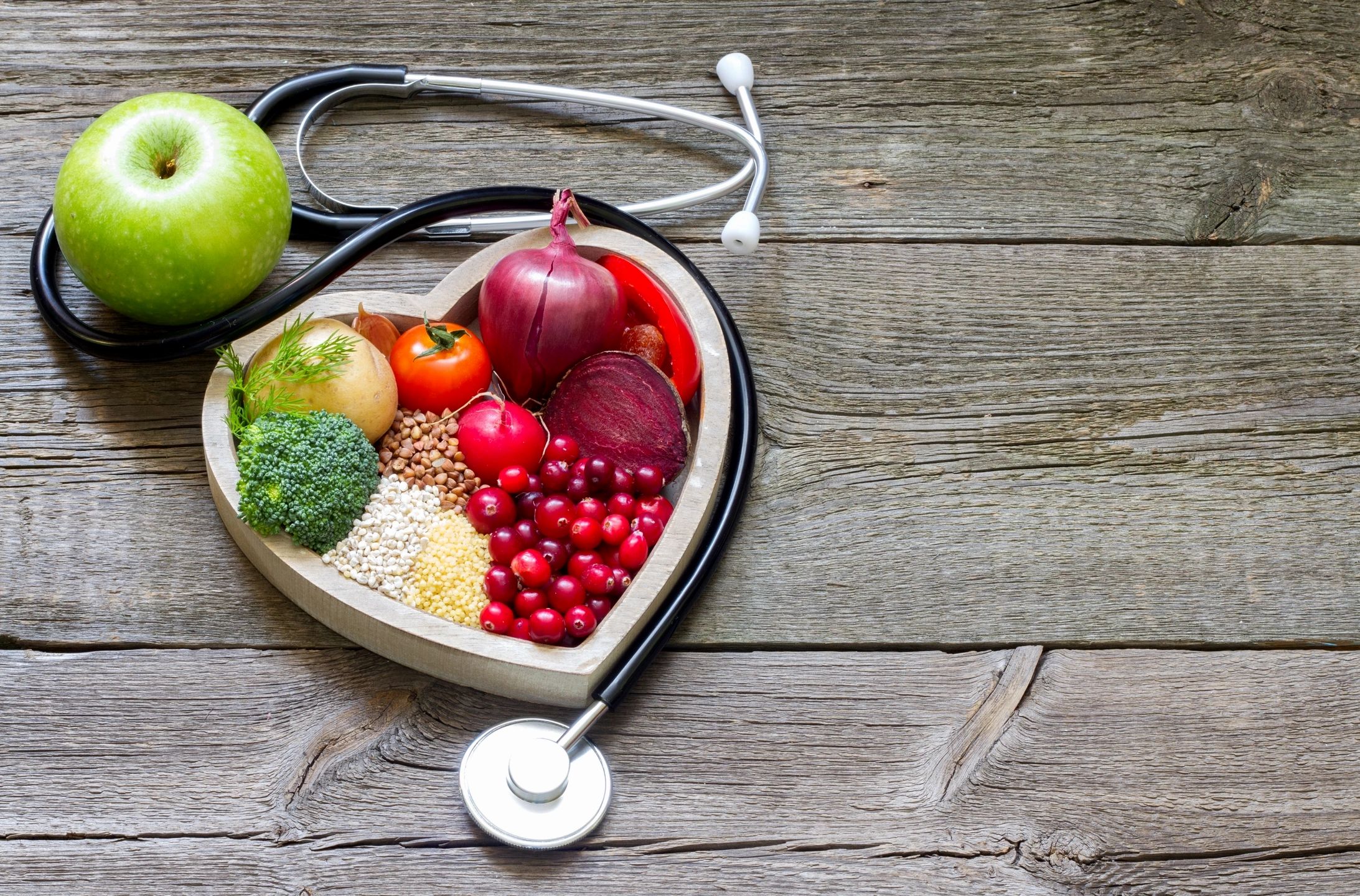 Healthy foods displayed in a heart shape wrapped with a doctor's stethoscope