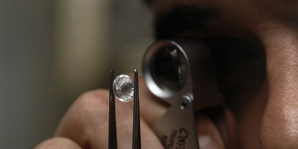 Man looking through magnifying glass at diamond held up by tweezers.
