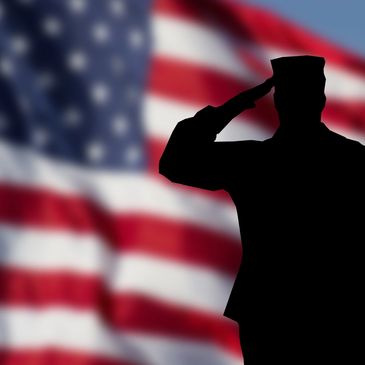 A silhouette of a saluting military member standing in front of an American flag 