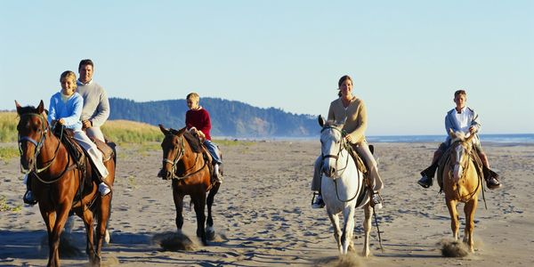 family horseback riding on the beach smiling
