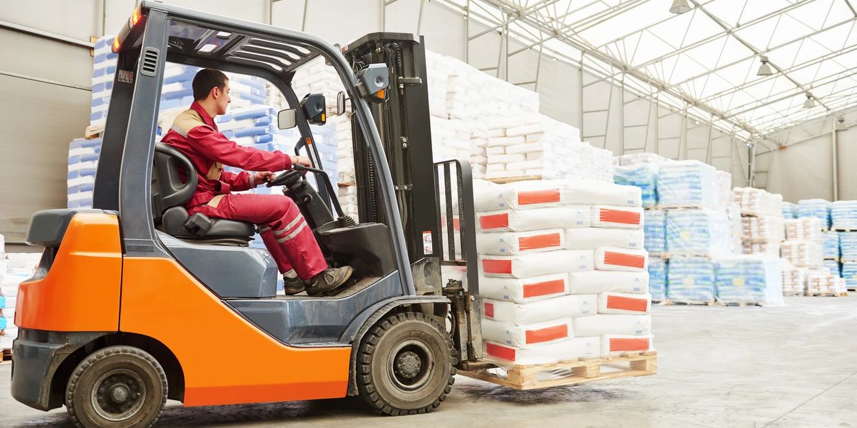 A man in a red jumpsuit drives a forklife in a warehouse. 