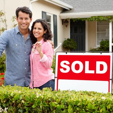 A couple standing in front of their new home next to a sold sign.