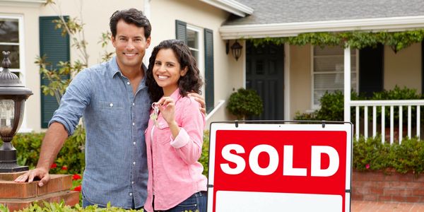 couple in from of house with sold sign 