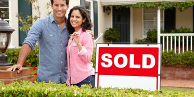 Couple with key in front of home with for sale sign.