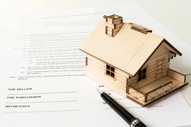 A small wooden house sits on real estate paperwork. We will help you figure out your closing! 