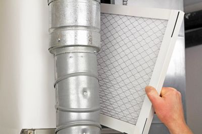 Person sliding a filter into an HVAC unit past ductwork