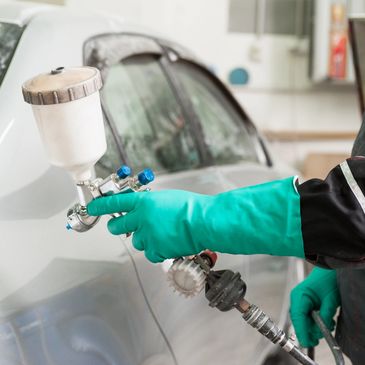 Auto body shop technician applying paint to automobile with spray-paint gun