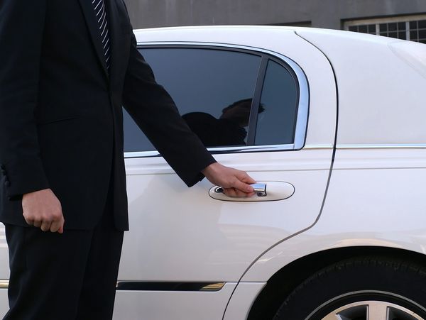 man in a suit opening a white car door