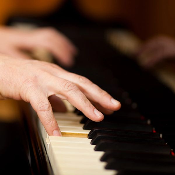 The image shows someone's hand playing an acoustic piano.