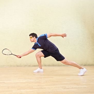 Squash player lunging to reach the ball and play his shot
