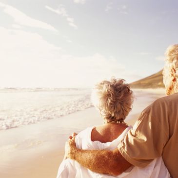 Older man and woman standing on the beach, staring out at the water.