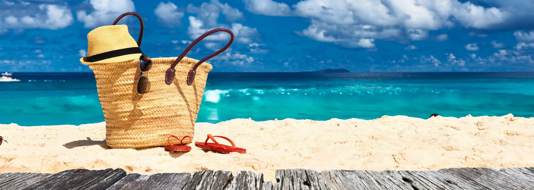 beach bag with straw hat on beach with tropical waters behind