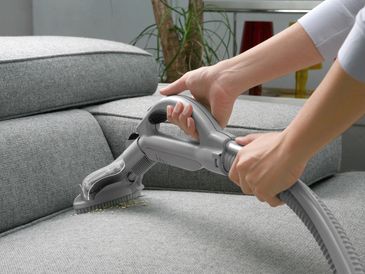 A professional vacuuming a sofa