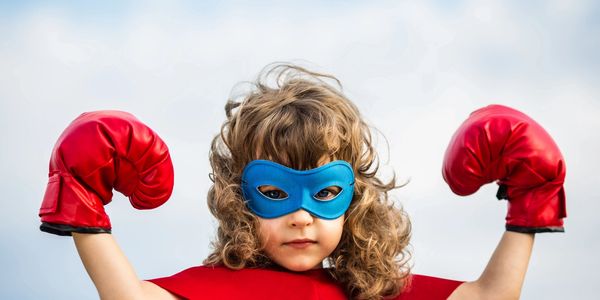 Girl dressed in a super hero costume and red boxing gloves, arms in a power position 