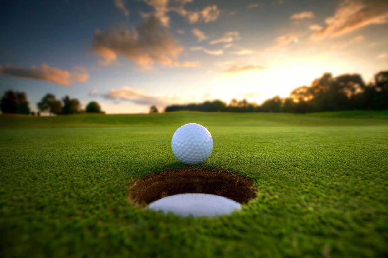 A golf ball rests on the golfing green, teetering on the edge of the hole.